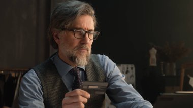 Tailor using tablet, transferring money on bank card, paying for service online during work in luxury atelier. Female tailor works on elegant suit on background. Fashion and entrepreneurship concept.