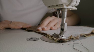 Hands of female seamstress works on sewing machine. Designer sews fabric in atelier sewing workshop. Concept of small business, tailoring industry, hand craft and fashion. Extreme Close-up shot.