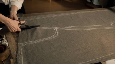 Professional female tailor cuts fabric according to sketch using scissors for sewing. Process of making clothes in luxury designer atelier or tailoring studio. Fashion and hand craft concept.