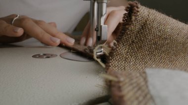 Hands of female seamstress works on sewing machine. Designer sews fabric in atelier sewing workshop. Concept of small business, tailoring industry, hand craft and fashion. Macro