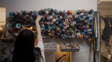 Fashion designer chooses color of threads for tailoring new wedding suit. Tailor takes skeins of threads while working on custom apparel. Mannequin and measure tapes at background. Concept of fashion.