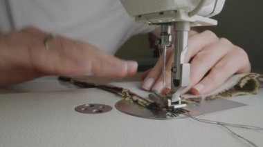 Hands of female seamstress works on sewing machine. Designer sews fabric in atelier sewing workshop. Concept of small business, tailoring industry, hand craft and fashion. Extreme Close-up shot.