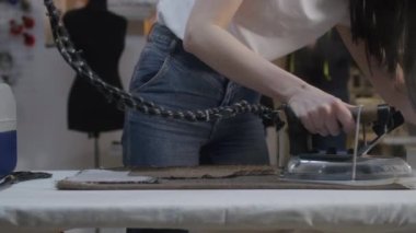 Woman irons fabric textile in atelier workshop. Her colleagues working on background: man works with tailored suit, seamstress works at sewing machine. Concept of fashion and hand craft.