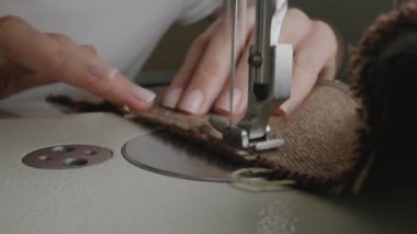 Hands of female seamstress works on sewing machine. Designer sews fabric in atelier sewing workshop. Concept of small business, tailoring industry, hand craft and fashion. Macro