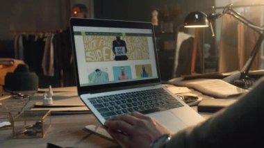 African American businessman in luxury designer atelier browsing online shop on laptop, watching clothing range, chooses sweatshirts. Concept of fashion and internet shopping. Close up view.