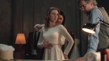 Cinematic shot of tailors taking measurements of woman for wedding dress. Bride on fitting wedding dress in luxury designer atelier or tailoring studio. Concept of fashion, handmade and couturier.