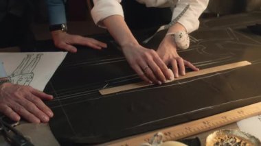 Male and female tailors transfer the sketch of future clothes to the fabric. They use ruler, soap and buttons. Luxury designer atelier or tailoring dim studio. Fashion, hand craft and handmade concept