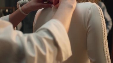 Close-up shot of tailor zipping up wedding dress on woman in front of mirror. Bride on fitting wedding dress in luxury designer atelier or wedding salon. Concept of fashion, handmade and couturier.