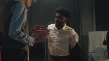 African American man on business wedding suit fitting in luxury atelier or tailoring workshop. Tailors and client discussing color and material of the vest. Concept of fashion and couturier.