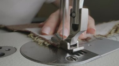 Hands of female seamstress works with fabric on sewing machine. Woman sews clothes in atelier workshop or at home. Concept of fashion, tailoring industry, handmade and self-employment. Close-up shot.