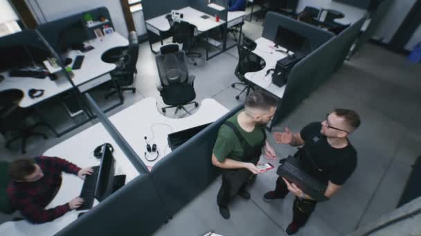 人们在现代化的办公室里工作 坐在有计算机的桌旁 机修工与员工交谈 建立并检查安全摄像头是如何与同事一起使用笔记本电脑的 安保摄像头拍摄 — 图库视频影像