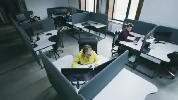 現代のオフィスで働いていて コンピュータとテーブルに座っている人々 女性はヘッドフォンを着用し 作業日を開始します 大人の男は修理Pcをもたらします It会社 同僚の概念 防犯カメラのショット — ストック動画