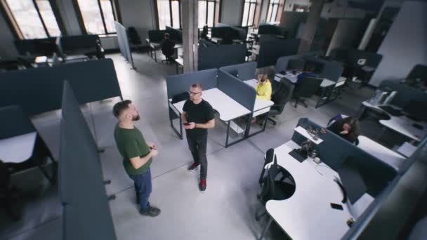 办公室里有现代设计的人 他们坐在有计算机的桌子旁边 同事讨论项目计划 人来到同事身边 帮助他完成工作任务 安保摄像头拍摄 — 图库视频影像