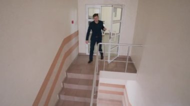 Zarif takım elbiseli başarılı bir adam kapıyı açar ve alt kattaki merdivenlerden iner. Modern iş merkezinin merdivenlerindeki iş adamları iş süreçleri arasında. Güvenlik kameraları ve CCTV.