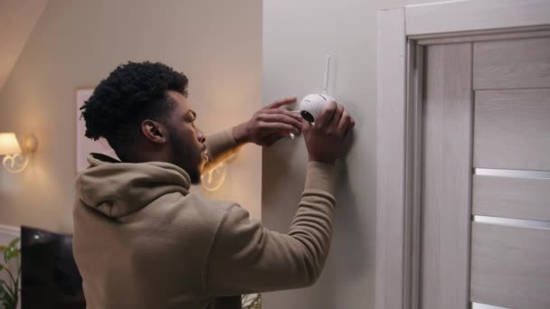 非裔美国人在墙上安装了摄像头 并用电线将其与系统连接起来 男人在家里装摄像头 闭路电视摄像头的概念 监控系统 安全和隐私 Dolly Shot — 图库视频影像