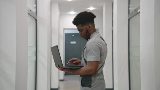 Üniformalı Afro Amerikalı Kurucu Koridorda Duruyor Dizüstü Bilgisayardaki Programı Kullanarak — Stok video