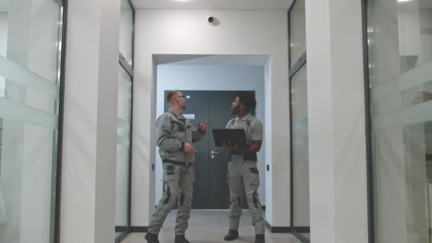 两个穿着制服的男人走在走廊上 讨论了在商务办公室安装闭路电视摄像头的问题 安装人员使用笔记本电脑上的计算机程序安装了安全摄像头 监测系统的概念 — 图库视频影像