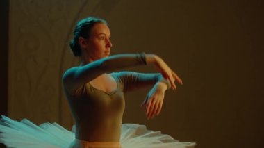 Cinematic shot of beautiful female ballet dancer on choreography rehearsal on theater stage, practicing elegant movements. Ballerina in ballet dress performs in opera. Classical theatrical ballet art.
