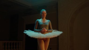 Cinematic shot of beautiful ballerina in ballet dress standing in theater hall and preparing to start the performance. Female dancer on choreography rehearsal in opera. Classical ballet art. Zoom in.