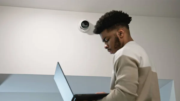 African american man sets up security cameras in office corridor using laptop. Installer checks CCTV cameras in computer program. Monitoring system. Concept of surveillance system and privacy.