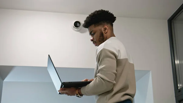 African american man sets up security cameras in office corridor using laptop. Installer checks CCTV cameras in computer program. Monitoring system. Concept of surveillance system and privacy.