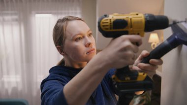 Caucasian repairwoman drills hole in concrete wall with drilling machine. Woman does repairs in her apartment. Repair work, installation of the Internet or making hole for the picture.