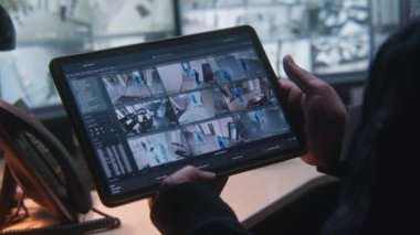Ofisteki kapalı devre kameraları erkek güvenlik görevlisi kontrol ediyor. Dijital tablet ve güvenlik kamerası görüntülü bilgisayarlar kullanıyor. Yüksek teknoloji güvenlik sistemi. İzleme ve sosyal güvenlik.