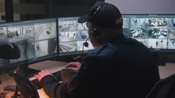 ヘッドセットのセキュリティガードは 夜にオフィスでCctvカメラを制御し コンピュータを使用します 監視カメラが画面上で再生されるハイテクソフトウェア 現代のセキュリティシステムと社会的安全コンセプト — ストック動画