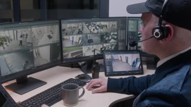 头戴耳机的安保人员控制着办公室的闭路电视摄像头 使用数字平板电脑 显示监控摄像头的高科技软件在屏幕上播放 社会安全的概念 — 图库视频影像