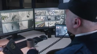 Güvenlik görevlisi ofiste yüz tanıma sistemi olan güvenlik kameralarını kontrol ediyor. Dijital tablet ve bilgisayar kullanıyor. Yüksek teknoloji yazılımı, güvenlik kameraları ekranlarda oynatıyor. Sosyal güvenlik kavramı.