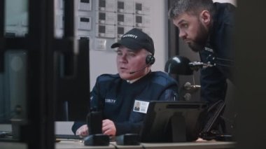 Adam iş arkadaşına geliyor, bilgisayar ve tablet monitörlerde görüntülenen güvenlik kameralarından bakıyor ve telsizle konuşuyor. Güvenlik görevlisi işyerinde oturup klavye çalıyor. CCTV teknolojisi.