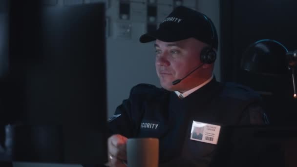 戴着耳机睡觉的安全官员坐在工作场所 从计算机显示器上显示的安全摄像头观看 男人喝一杯咖啡 监测和跟踪系统 闭路电视技术 — 图库视频影像