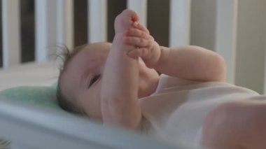 Beyaz çarşaflı, çocuk karyolasında yatan beyaz takım elbiseli küçük beyaz çocuğu yakından çek. Sevimli ve tatlı çocuk oynuyor ve kameraya bakıyor. Bebek, çocukluk, ebeveynlik, hayat ve aile kavramı.