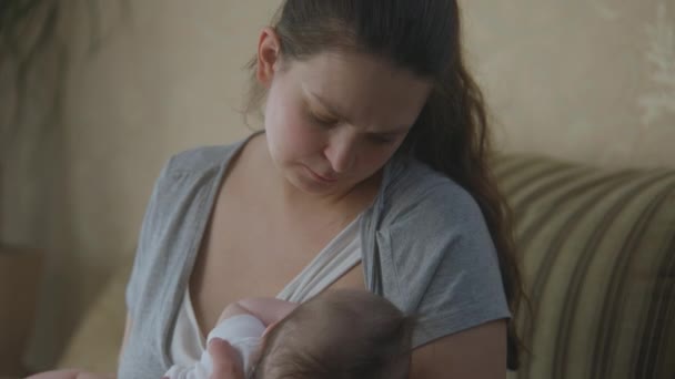母親の母乳育児自宅でソファに座っている小さな新生児 女は娘や息子を腕に抱え 赤ん坊を眠らせる 子供時代 母親時代 愛と家庭の概念 スローモーション — ストック動画