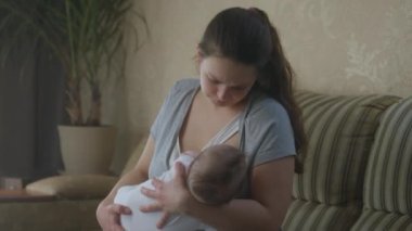 Bakıcı anne, evdeki kanepede oturan küçük bebeği emziriyor. Kadın, anne sütüyle beslenen kız ya da çocuğu kollarında tutuyor. Çocukluk kavramı, annelik, sevgi ve aile..