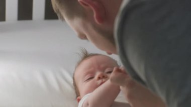 Mutlu babanın bebekle oynadığı yakın plan çekimler, sabahları çocuk alnından öpmeler. Bedenli küçük bir kız ya da erkek çocuk karyolasında yatıyor. Çocukluk kavramı, ebeveynlik, sevgi ve aile. Yavaş çekim.