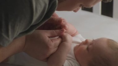 Mutlu baba sabah beşikte şirin bebekle oynar, küçük ellere dokunur ve öper. Yeni doğmuş bir bebek beyaz çarşafların üzerinde yatıyor. Çocukluk kavramı, ebeveynlik, yaşam, aşk ve aile.