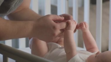 Çocuk beşiğinde sevimli bebekle oynayıp ellerini tutan mutlu babayı yakından çek. Sabahları beyaz çarşafların üzerinde küçük bir kız ya da erkek çocuk yatıyor. Çocukluk, ebeveynlik ve aile kavramı.