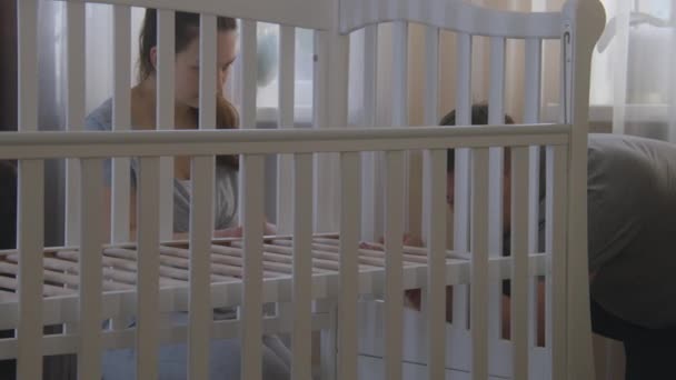 保育園で赤ちゃんのための白いベビーベッドを組み立て親を愛する 父は赤ん坊の揺りかごを固定するために16進キーを使用する 介護妻は愛する人を助ける 家族の概念 — ストック動画