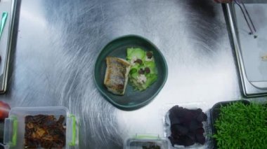 Erkek aşçı servis için yemek kompozisyonu yapar. Şef, kızarmış balık ve buğulanmış sebzelerle yemek sunumu yapar ve onu böğürtlenlerle süsler. Profesyonel gurme mutfağı olan bir restoran..