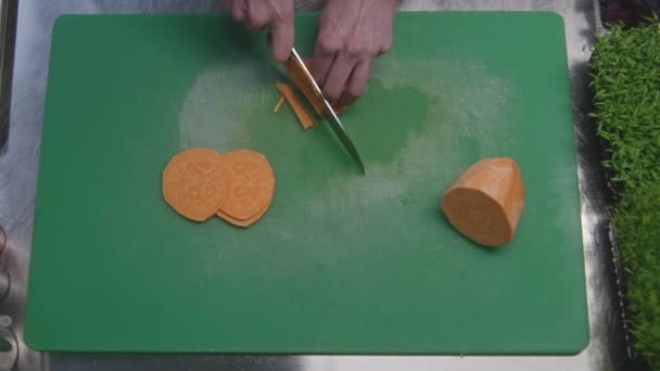男性の調理は まな板の上の小さな断片にサツマイモをカット プロのシェフの手を閉じる キッチン机の上の緑と野菜 プロの料理とレストラン ベジタリアン料理 — ストック動画