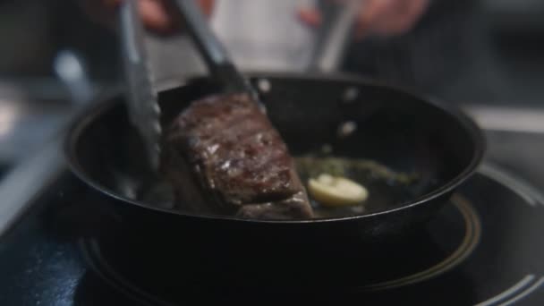 シェフはストーブの上でおいしい食事を調理します 男性はローズマリーやニンニクでフライパンにフライドポテトジューシーな牛肉肉を調理し キッチン用品を使用しています ローストステーキ料理のプロセス プロのキッチン付きレストラン — ストック動画