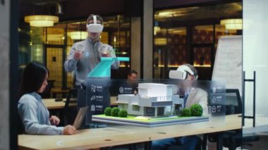 Erkek tasarımcı sanal gerçeklikte iş arkadaşlarına akıllı ev tasarım projesini sunan VR kulaklık ve kablosuz kontrol cihazları kullanır. Modern yüksek teknoloji şirketi. Üç boyutlu hologram. Gelecekteki dijital teknolojiler.