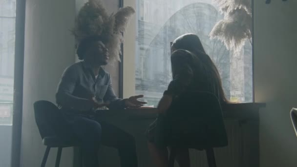 Afroamerikansk Man Sitter Vid Bordet Nära Fönstret Gestikulerar Och Pratar — Stockvideo