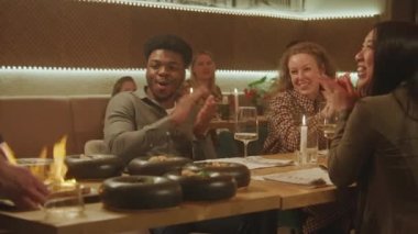 Şef modern gastro kafede insanların önünde flambe tarzı yemek hazırlıyor. Neşeli çoklu etnik arkadaşlar hafta sonunu restoranda doğum günü partisinde geçirirler. Toplu yemek kavramı.
