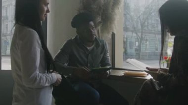 Afro-Amerikalı erkek ve Asyalı kadın ellerinde menüyle pencerenin yanındaki masada oturuyor ve sipariş veriyorlar. Bayan garson konuklarla konuşuyor. Kafede buluşan çok ırklı bir çift. Toplu yemek kavramı.