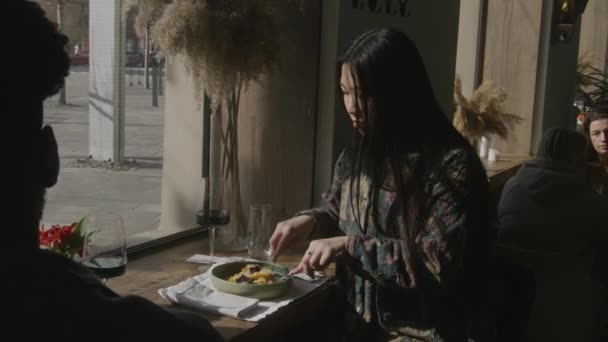 亚洲女人坐在靠窗的桌旁 吃午饭 和非洲裔美国男人交谈 具有现代设计的餐厅里的多民族客人 美味的美味佳肴 公众饮食的概念 — 图库视频影像