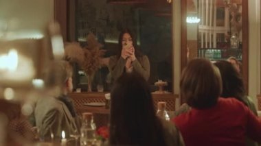 Asyalı kadın, modern gastro kafede arkadaşlarıyla telefon kullanarak fotoğraf ve selfie çekiyor. Bir grup insan hafta sonu akşamını restoranda doğum günü partisinde takılarak geçiriyor. Kamu hizmeti kavramı.