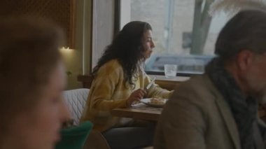 Genç bir kadın modern kafede masada oturuyor, lezzetli yemekler yiyor, dizüstü bilgisayarla serbest çalışıyor. Serbest çalışan bir kadın restoranda yemek yer, garsonla konuşur, sipariş verir. Toplu yemek kavramı.