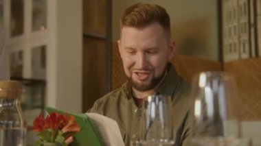 Yetişkin adam arkadaşlarıyla konuşur, menüyü izler ve siparişi verir. Garson, modern tasarımı olan bir restoranda konuklara servis yapıyor. Şarap kadehleri ve çiçekler masanın üzerinde duruyor. Toplu yemek kavramı. Dikey görünüm.